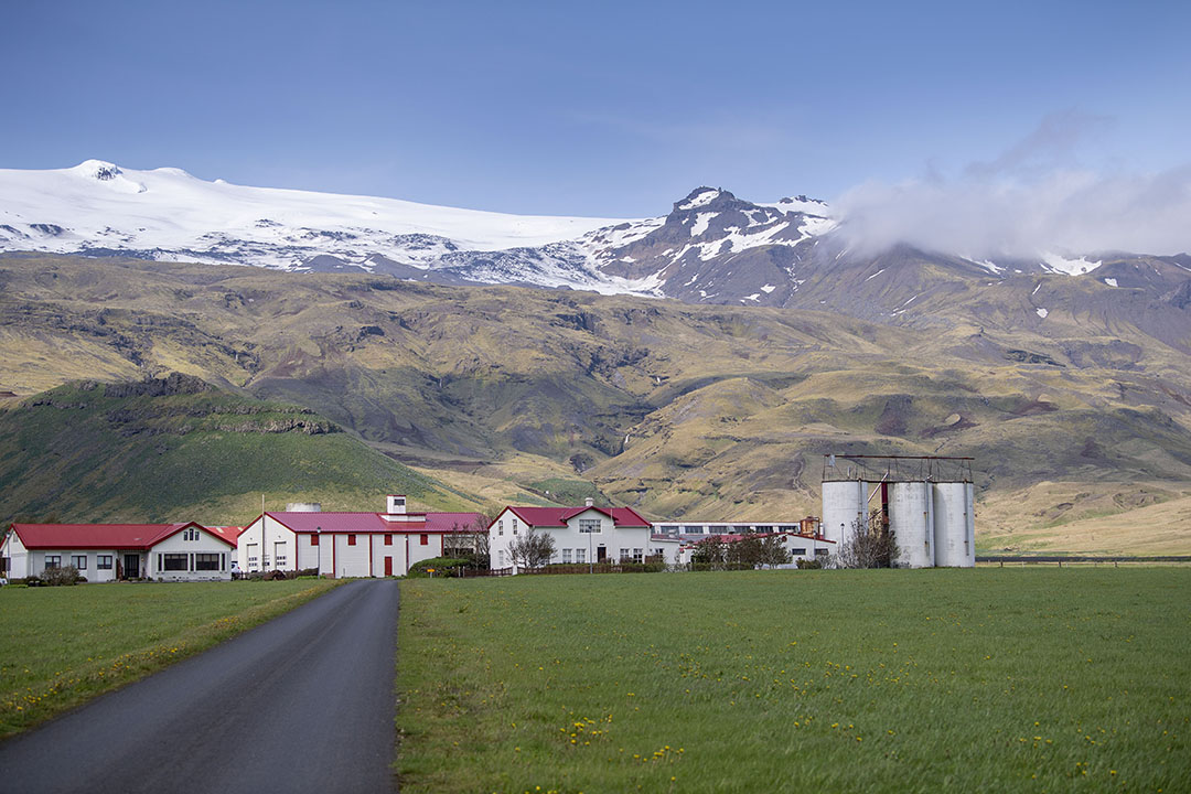 Een vooraanzicht van het bedrijf van Páll ´Olafsson, met helemaal rechts drie torensilo’s waar gras in wordt opgeslagen. Op de achtergrond zijn bij helder weer de Eyjafjallajökul-vulkaan en gelijknamige gletsjer te zien.