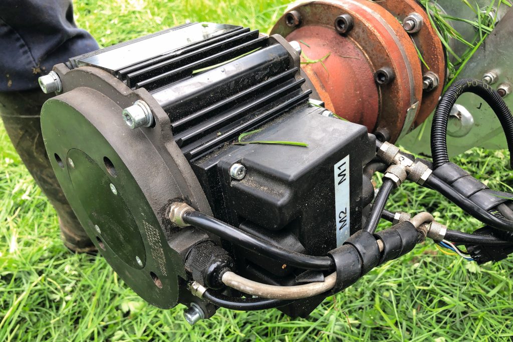 Eén van de drie elektromotoren. Rechts ervan is de tussenkast te zien om het juiste toerental te hebben voor het maaimechaniek. Voorop zie je de kabel (midden), de sensorkabel (onder) en de slang voor de waterkoeling.
