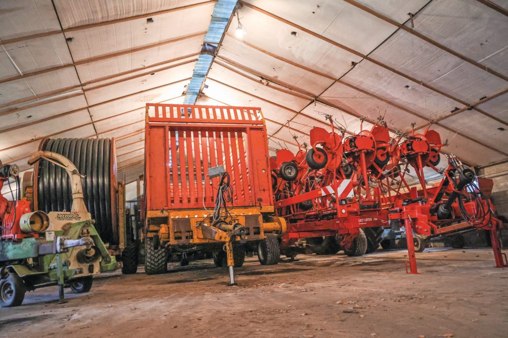 In een gehuurde winterstalling staan de werktuigen, waaronder drie beregeningshaspels. Het is op de zandgrond waarop Van Helmond boert niet uitzonderlijk dat ze allemaal tegelijk draaien om de groei in het gras te houden.